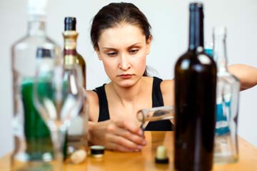 женщина сидя за столом наливает алкоголь в стакан