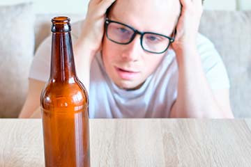 мужчина сидит рядом с бутылкой пива и держится за голову