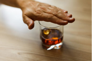 Человек накрыл рукой стакан с алкоголем